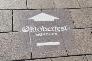 Die Folien mit dem Schriftzug Oktoberfest und einem Pfeil werden auf den Gehsteigen angebracht.